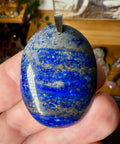 Blue stone pendant held in a hand with a blurred background