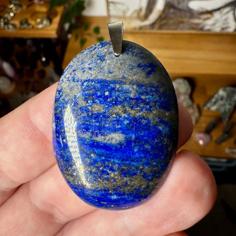 Blue stone pendant held in a hand with a blurred background
