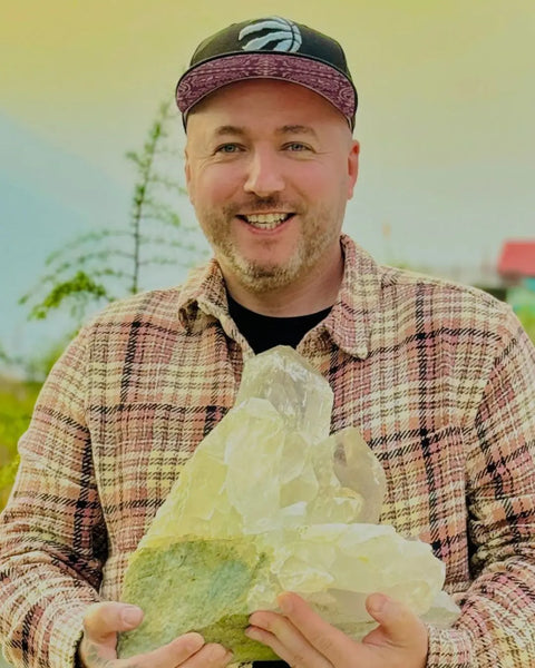 Man holding a large crystal formation outdoors with a blurred natural background