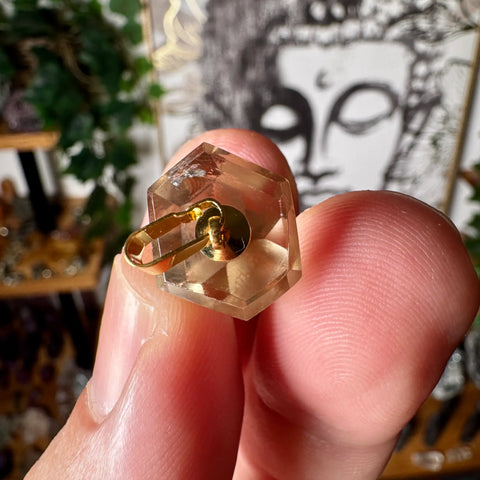 Citrine with a hexagonal top held between fingers against a blurred background