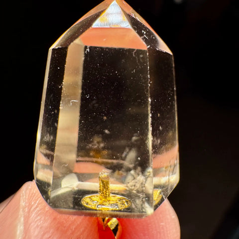 Citrine crystal held between fingers with a dark background